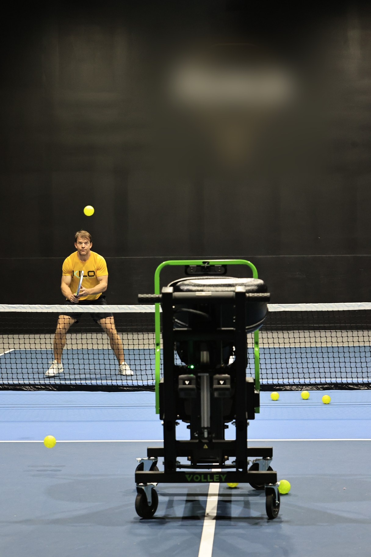 A member in ready position rallies against the Volley trainer across the net on an indoor court