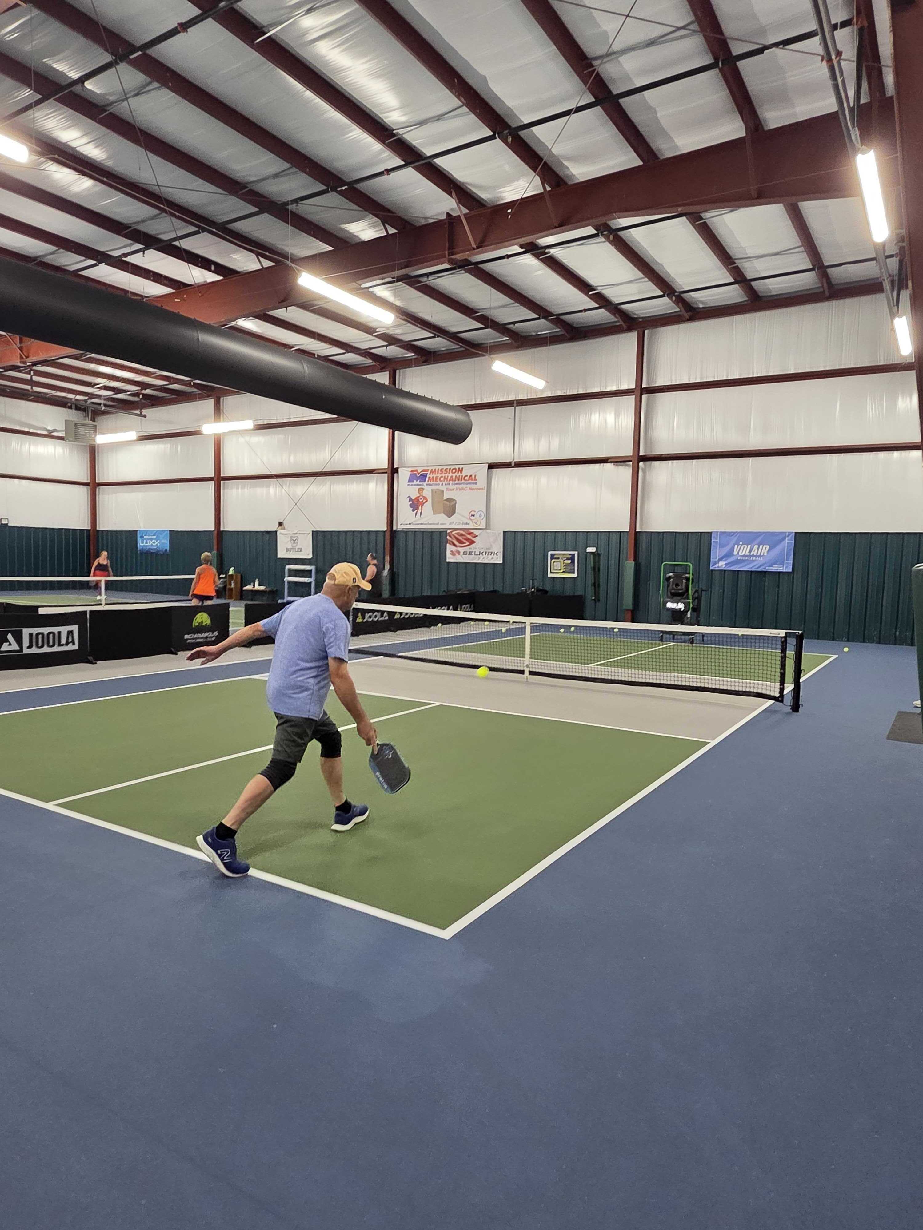An IPC member mid-rally during open play, with a Volley trainer standing courtside ready for the next player to run their own assessment